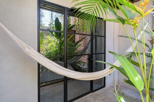 Una hamaca atada entre dos ventanas, un muro de ladrillo y una planta en maceta.