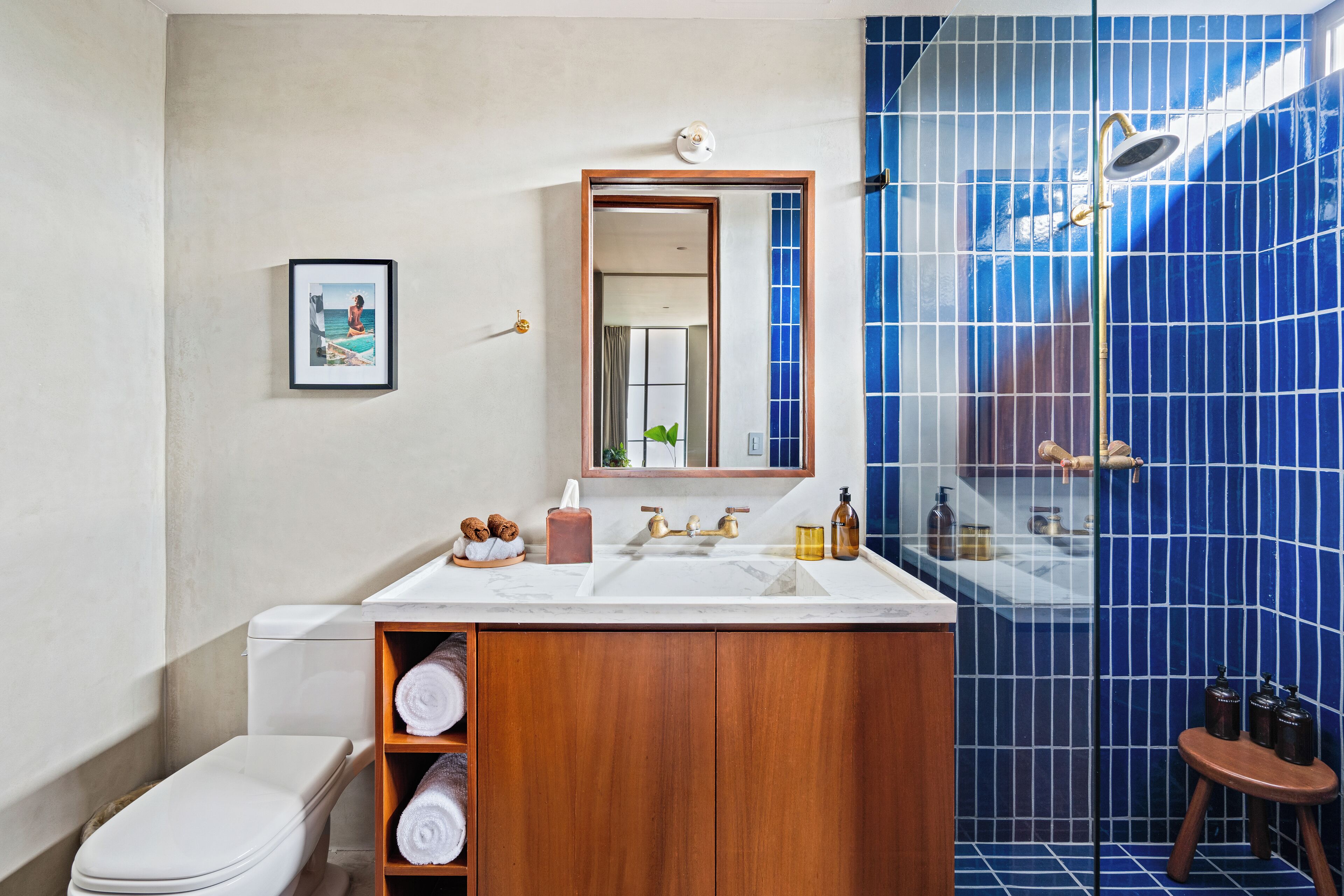 A bathroom with a wooden vanity, a white sink, a mirror, and a blue-tiled shower area.