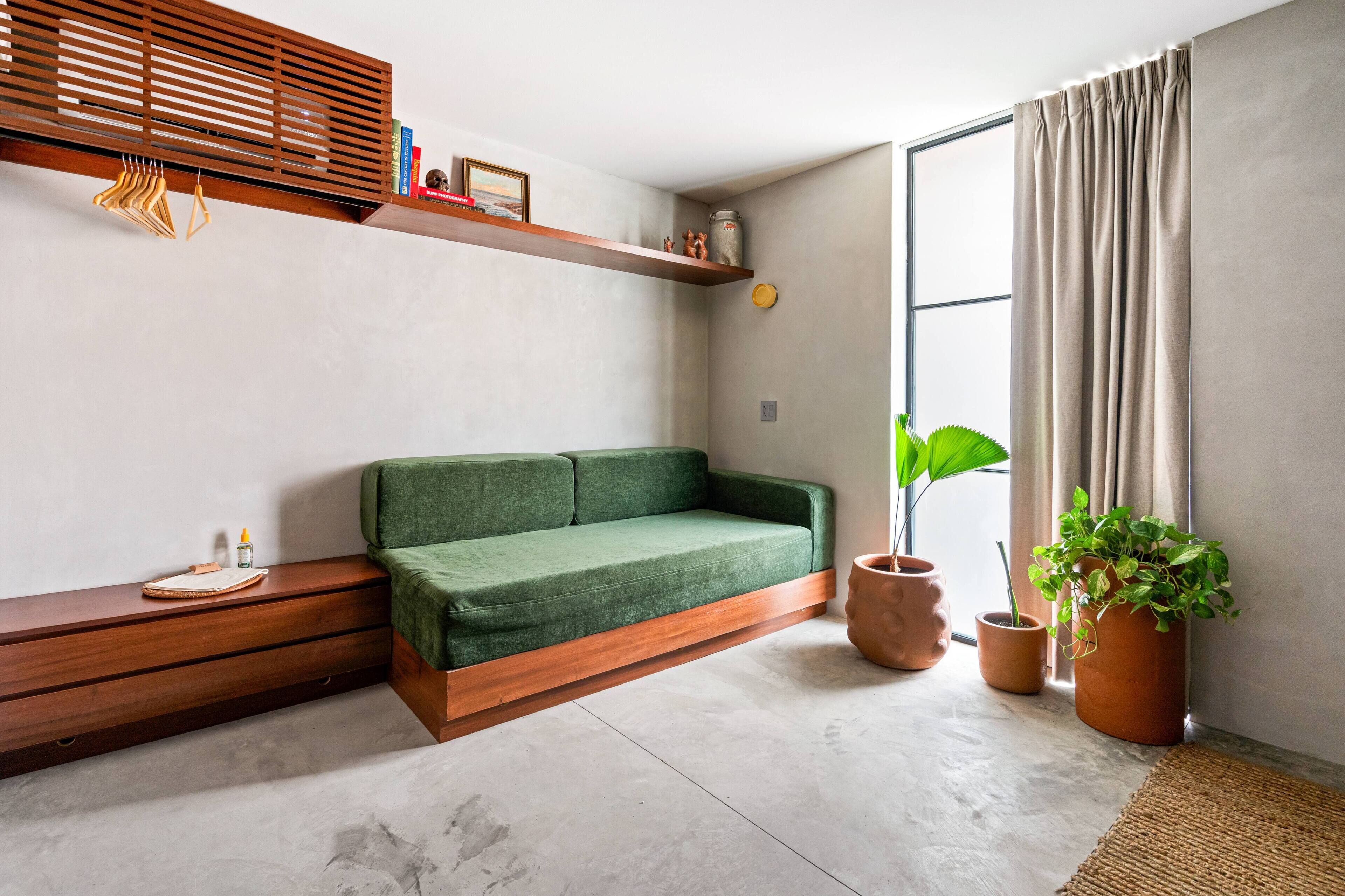 A modern living room with a green sofa, wooden shelves, potted plants, and a large window with curtains.
