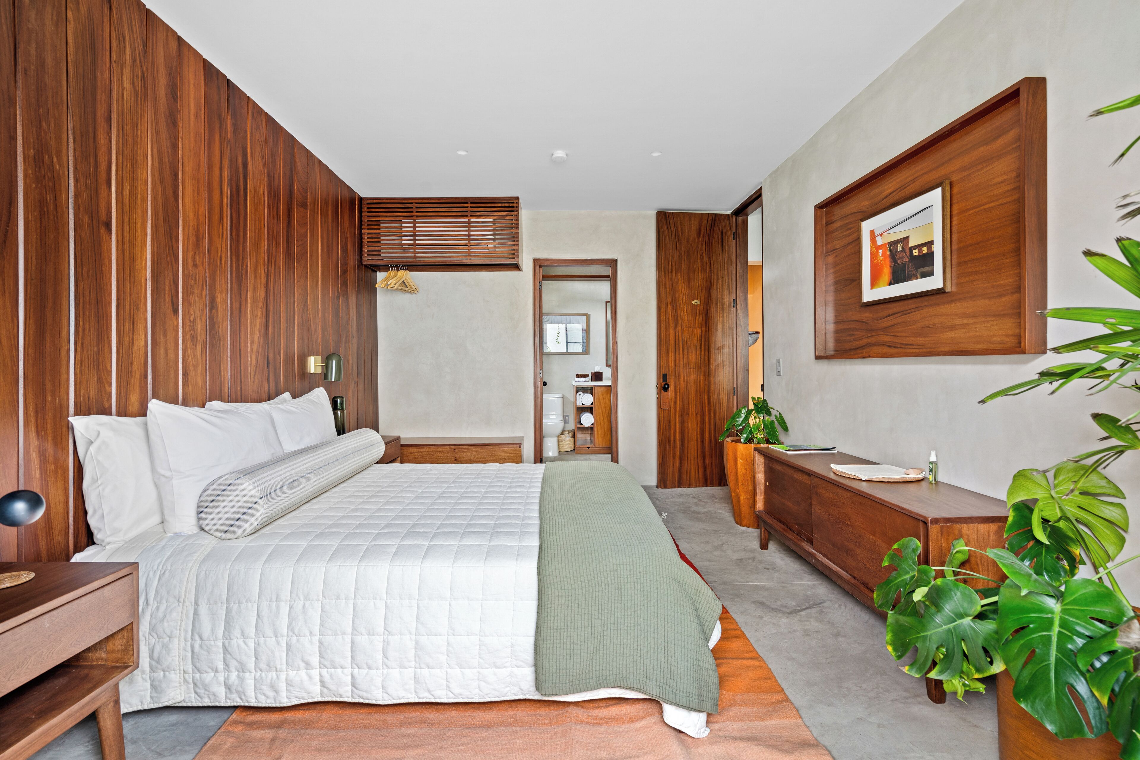 Ein modernes Schlafzimmer mit einem großen Bett, Holzwandverkleidung, einer Holzkommode und einem großen Fenster.