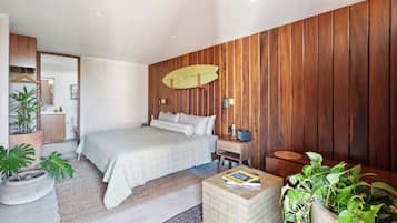 Ein Schlafzimmer mit einem Bett, Holzwandverkleidung, einem Surfbrett, einem Nachttisch und Topfpflanzen.