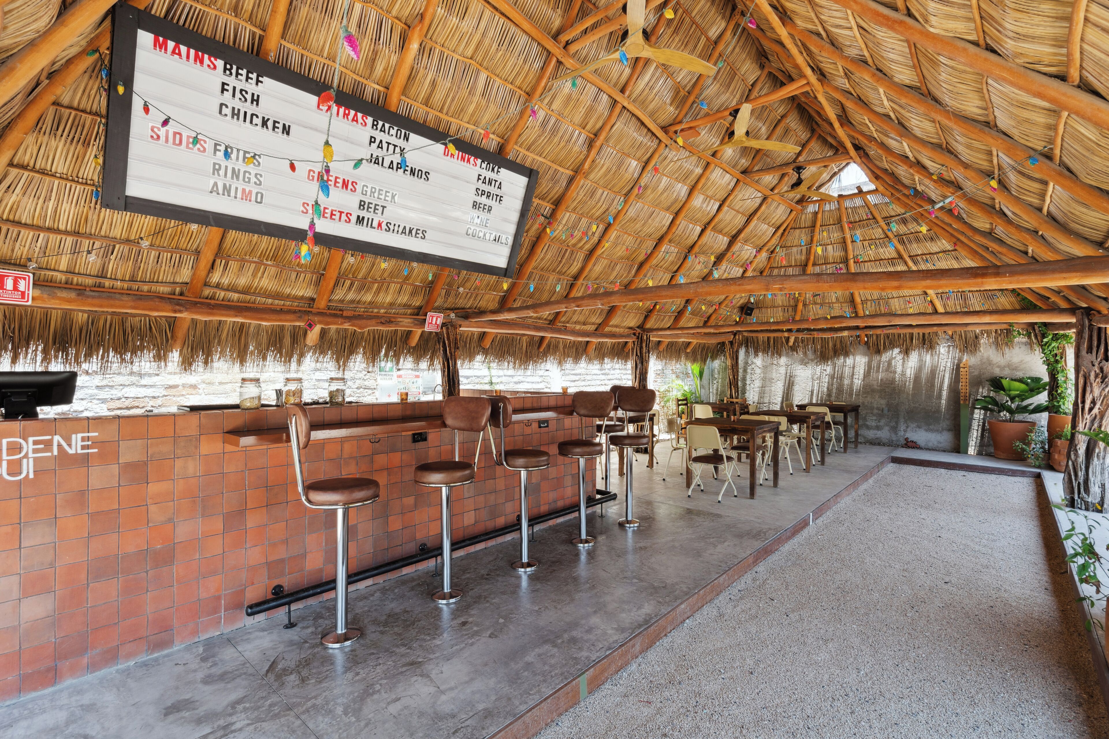 Una zona de bar con una pizarra de menú, taburetes y un techo de paja.