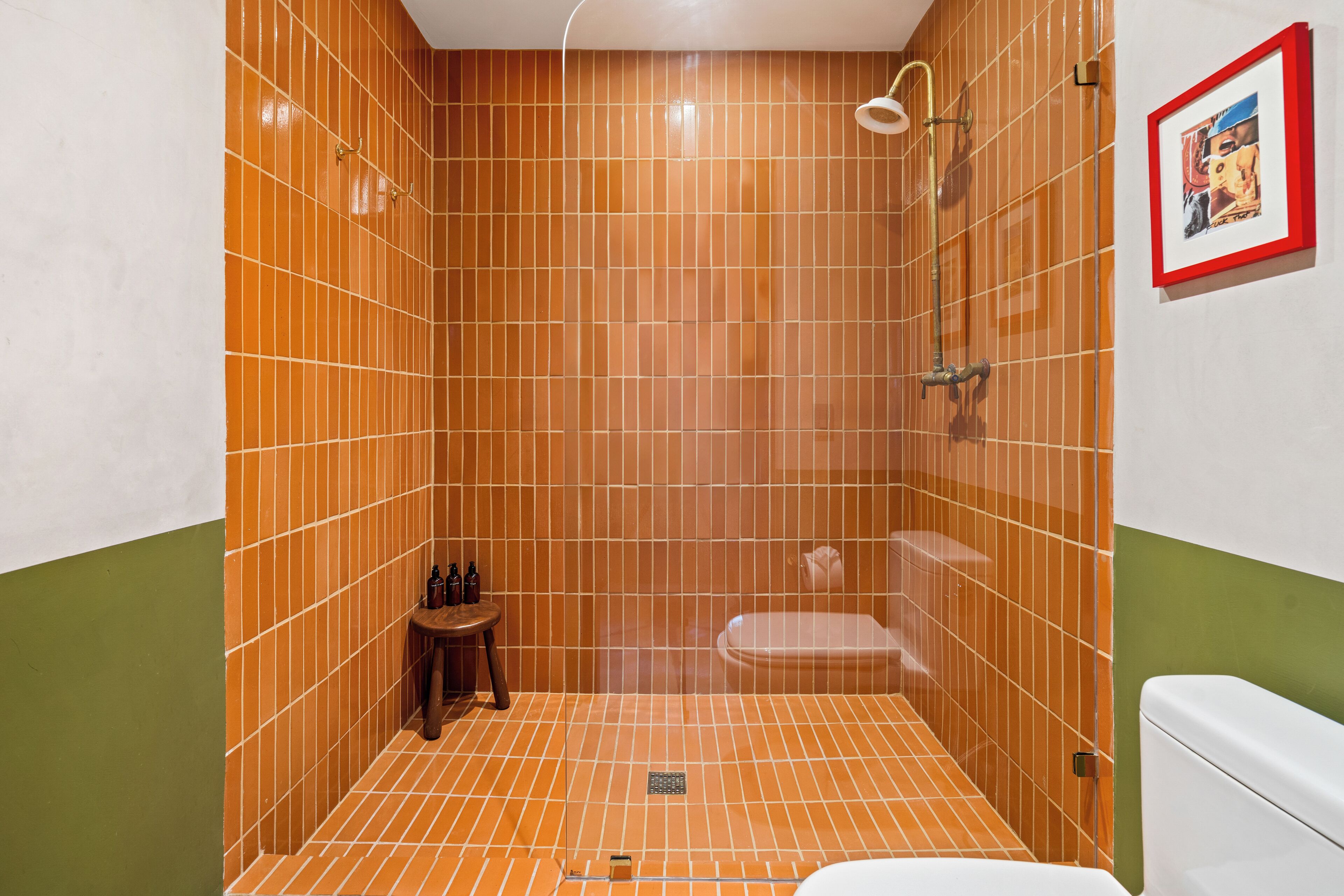 Baño con paredes de azulejos anaranjados, un inodoro blanco y una zona de ducha.