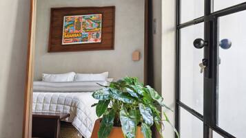 Un dormitorio con un espejo grande que refleja una cama, una planta en maceta y una obra de arte colgada en la pared.