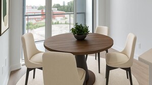 Een moderne eetruimte met een ronde tafel, vier stoelen, een plant in het midden en grote ramen met uitzicht op de stad.