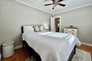 A bedroom with a bed, a ceiling fan, a dresser, and a trash can.