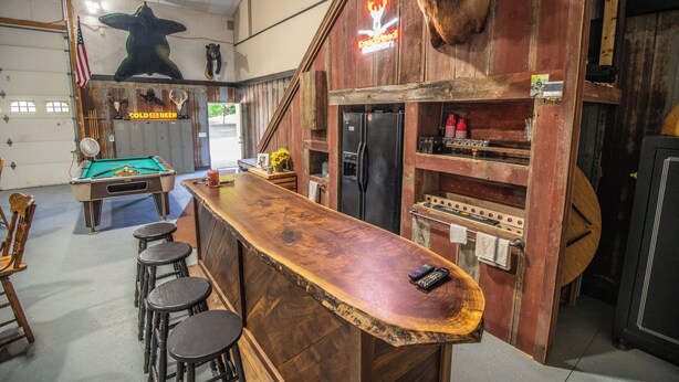 Un área de bar con mesa de billar, taburetes y un refrigerador.