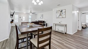 A spacious dining area with a wooden table and chairs, a ceiling fan, and a chandelier.