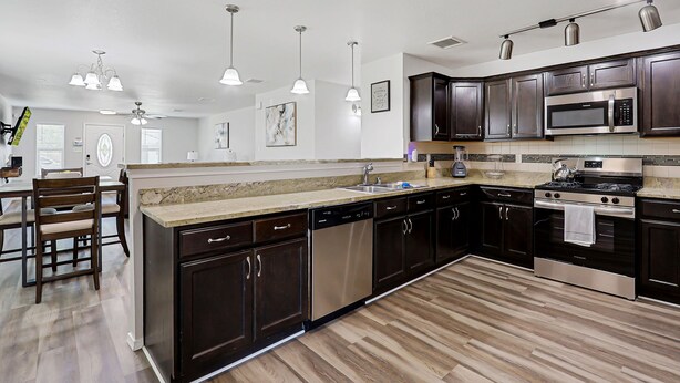 A modern kitchen with dark wood cabinets, stainless steel appliances, and a large island with a sink.