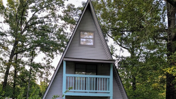Una casa triangular con balcón, rodeada de árboles.