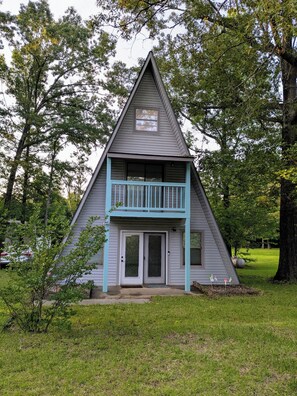 Una casa triangular con balcón, rodeada de árboles.