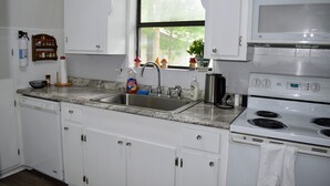 Una cocina con armarios blancos, un lavamanos de acero inoxidable, un microondas y una estufa.