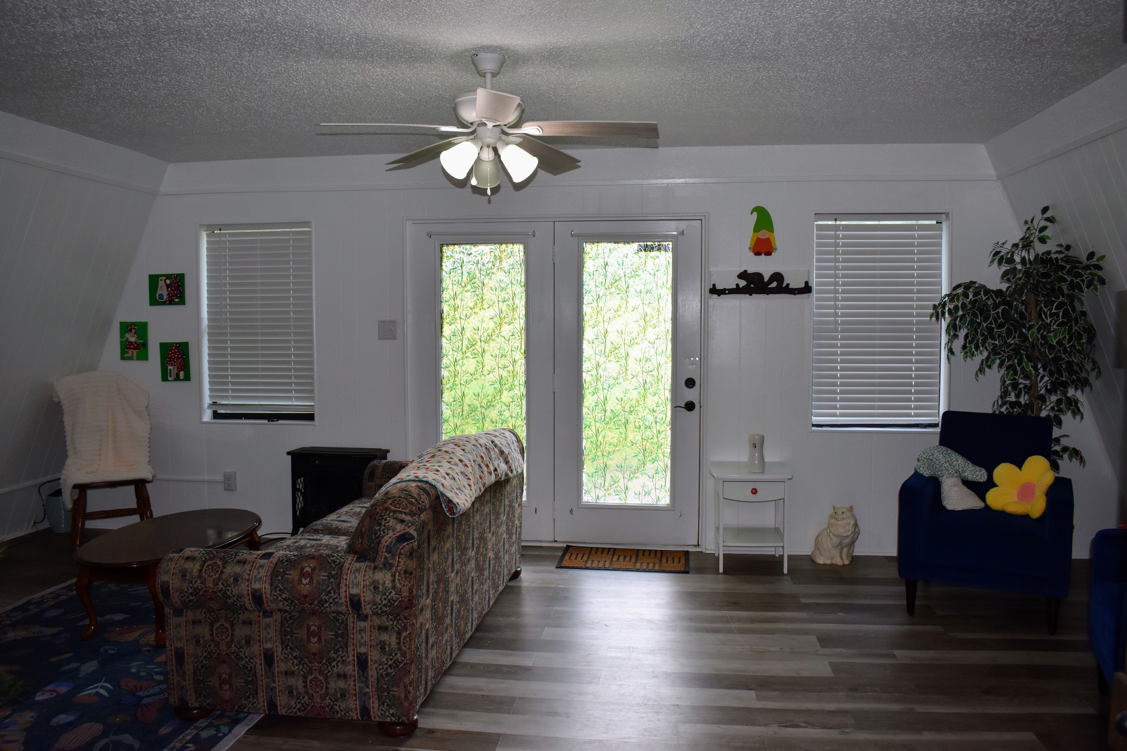 A living room with a patterned sofa, a blue armchair, a ceiling fan, and a potted plant.