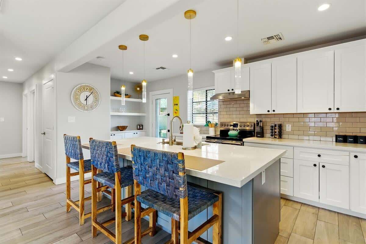 A modern kitchen with white cabinets, a central island with bar stools, pendant lighting, and a visible clock.
