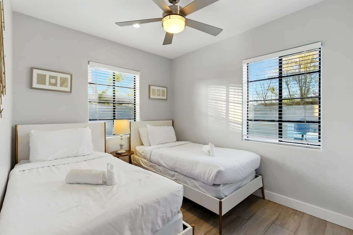 A hotel room with two beds, a ceiling fan, and large windows with blinds.