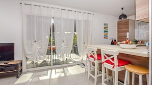 Una cocina moderna con comedor, televisor y un amplio ventanal con cortinas traslúcidas.