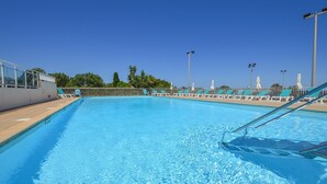Una piscina con agua azul cristalina, rodeada de sillas de descanso y sombrillas, bajo un cielo despejado.