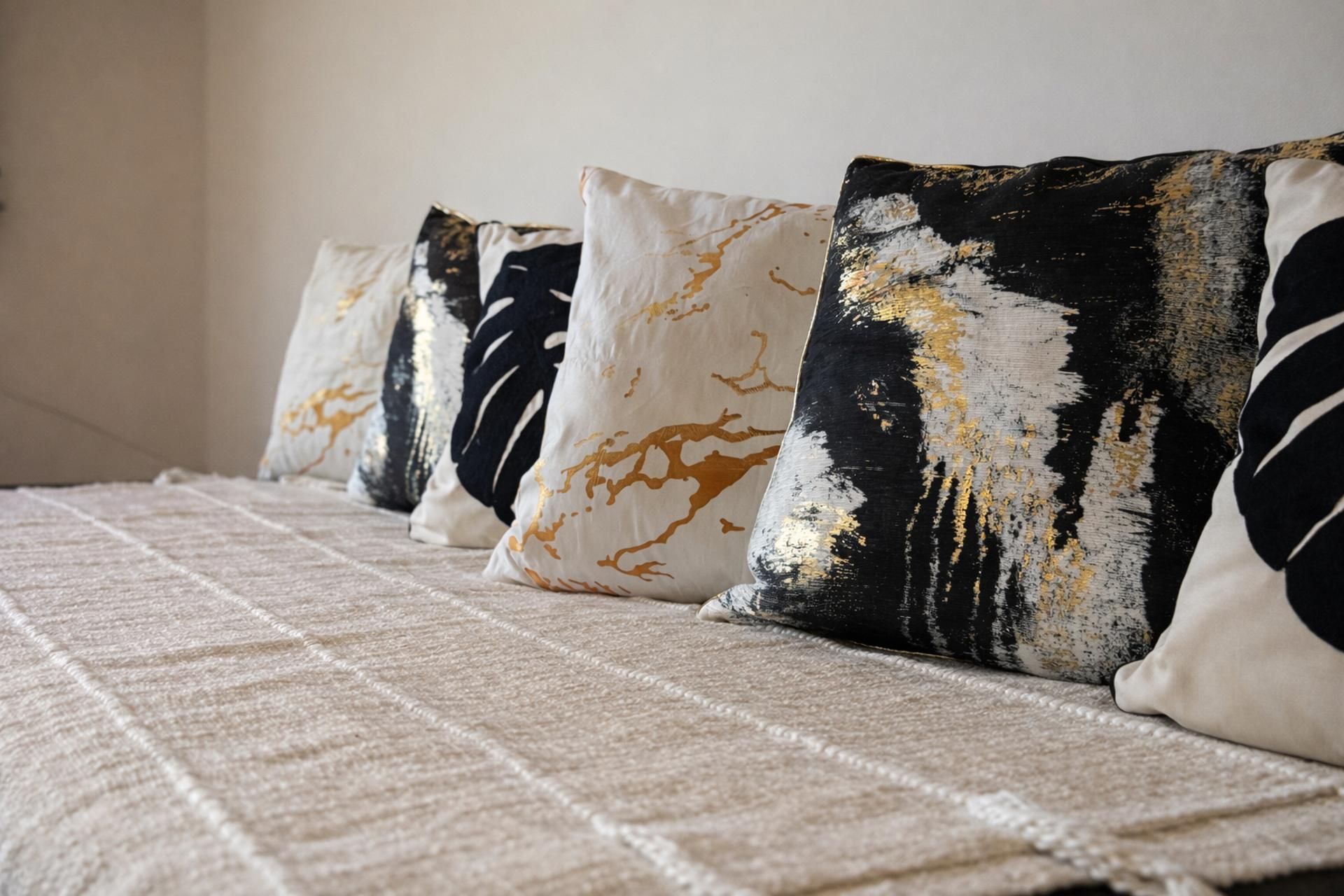 A bed with a textured beige bedspread and a row of decorative pillows with abstract patterns.