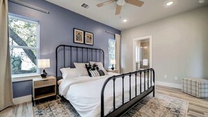 Une chambre à coucher avec un lit, des tables de chevet, un ventilateur de plafond et une vue sur l’extérieur.