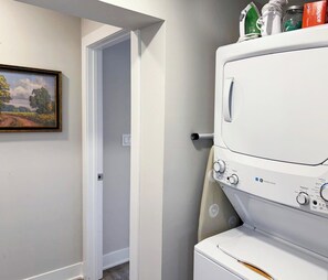 A laundry room with stacked washers and dryers, a door leading to another room, and a landscape painting on the wall.