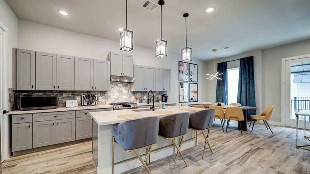 A modern kitchen with white cabinets, a central island with bar stools, and pendant lighting.