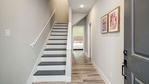 A staircase with white railings and dark steps leading to a bedroom with a bed and a light-colored wall.