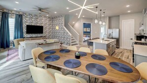 A modern living room with a dining area, a kitchen, and a staircase.