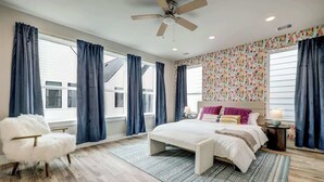 A bedroom with a large bed, a fluffy chair, a ceiling fan, and a patterned wall.