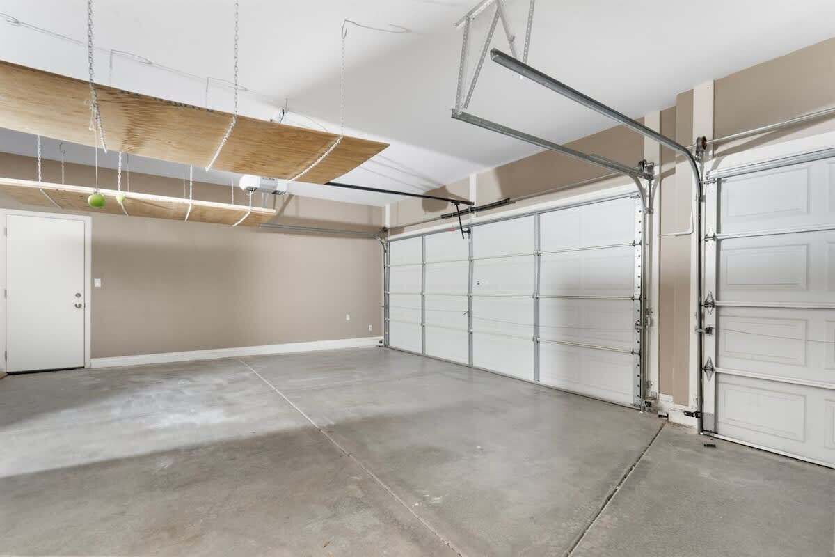 A garage with two white garage doors, a concrete floor, and a wooden ceiling with exposed beams.