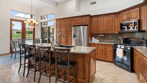 A kitchen with wooden cabinets, stainless steel appliances, and a large island with bar stools. - Lakeside home with private patio, Grill, Golf view (Glendale)