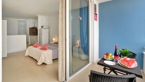 Une chambre avec un lit, une table garnie de nourriture et de boissons, et une porte-fenêtre coulissante donnant sur un balcon.