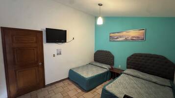 A room with two beds, a television mounted on the wall, a painting, and a wooden door.