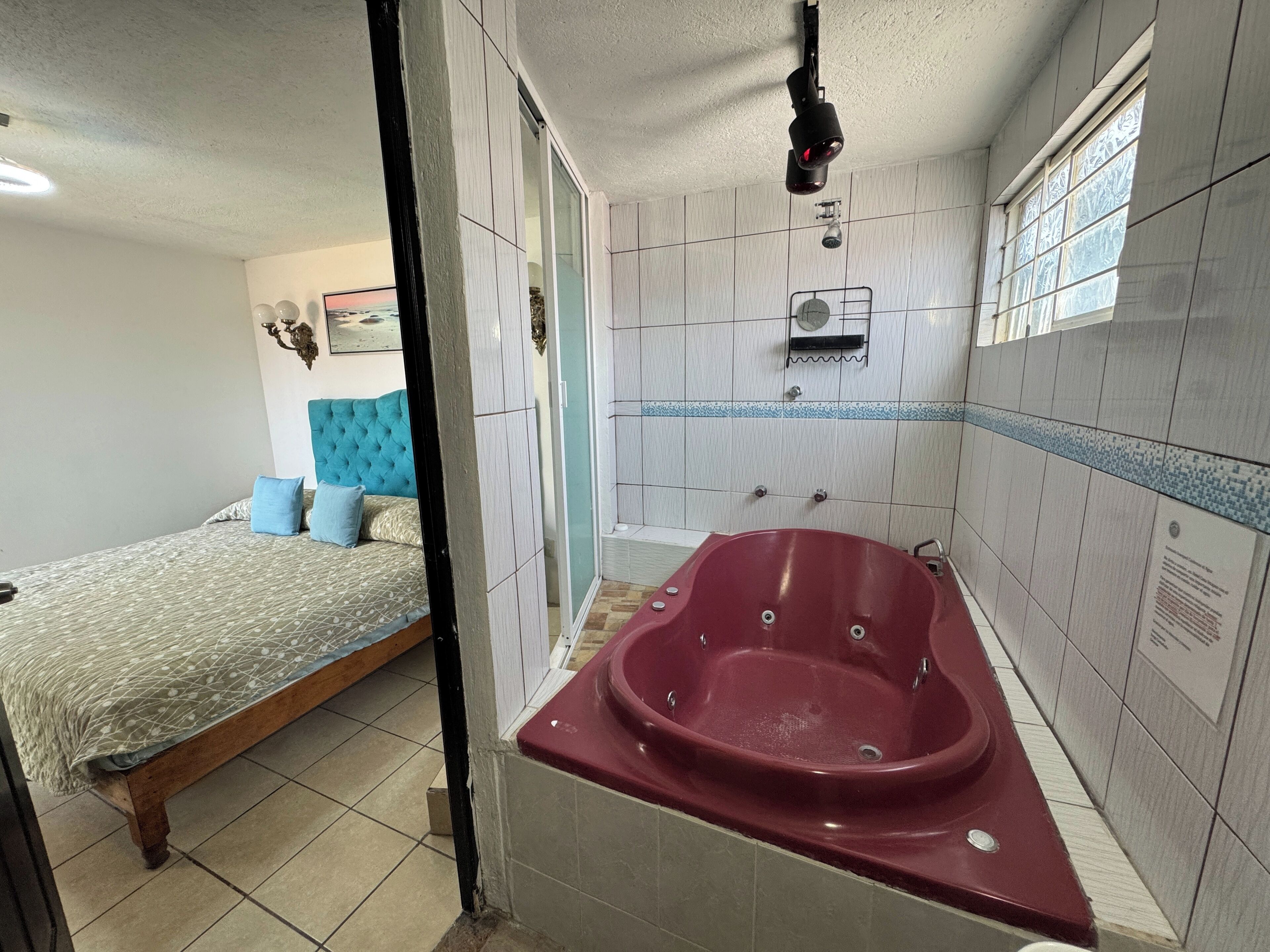 A bedroom with a bed, a red bathtub, and a window.