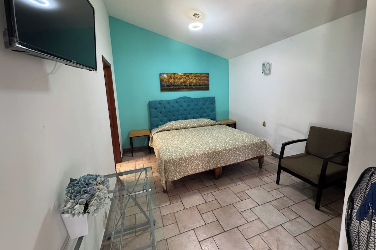 A bedroom with a bed, a chair, a TV, and a painting on the wall.