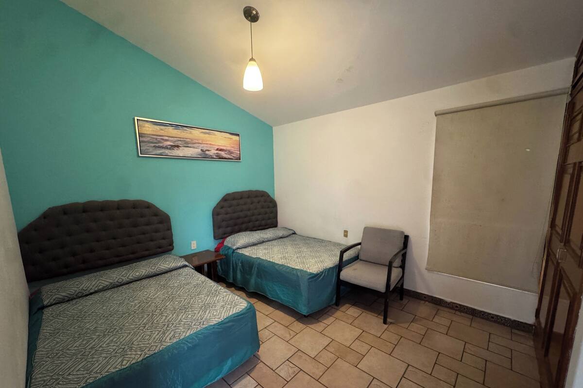 A small, tidy room with two beds, a chair, and a large window.