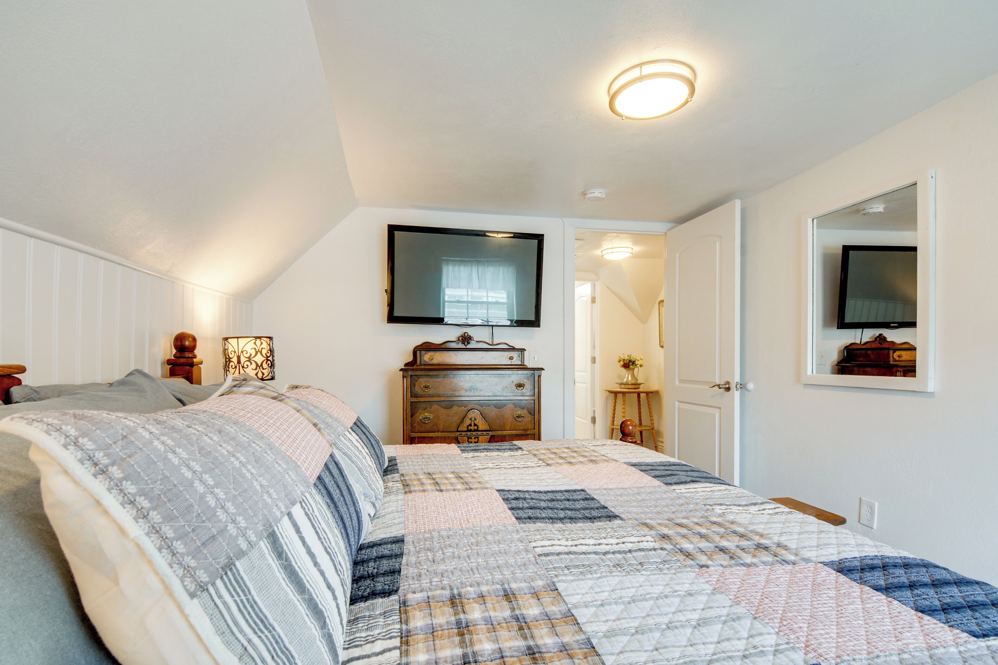 A bedroom with a bed, a dresser, a mirror, and a television.