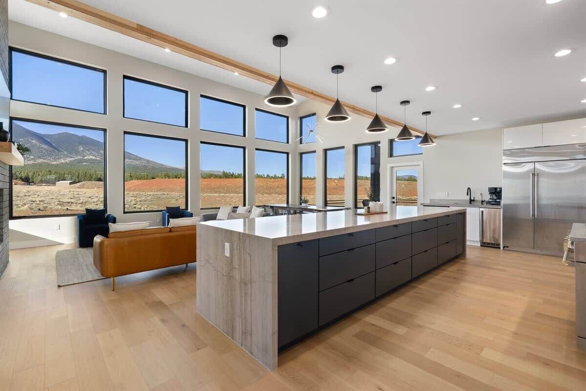 A modern kitchen with large windows, a central island, and a view of a mountainous landscape.