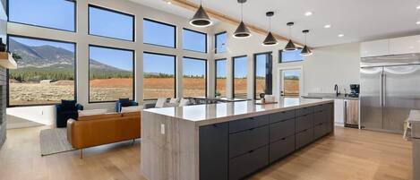 A modern kitchen with large windows, a central island, and a view of a mountainous landscape.