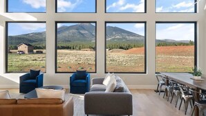 A living room with large windows, a sofa, chairs, and a dining area. - The Bluebird Flagstaff, Jacuzzi, Sleeps 26 (Flagstaff)