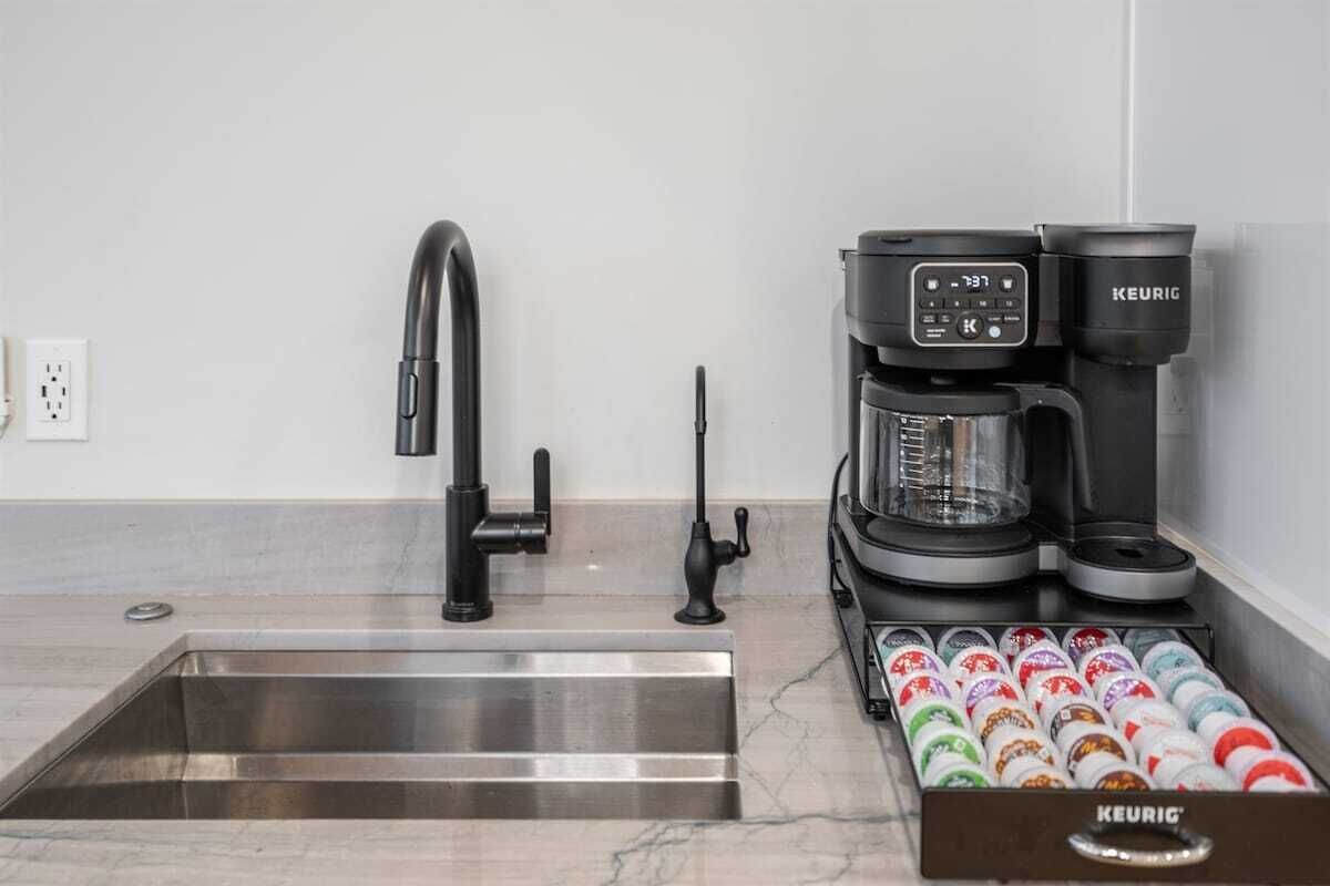 Eine moderne Küche mit einem Edelstahlspülbecken, einem schwarzen Wasserhahn, einer Keurig-Kaffeemaschine und einer Schublade voller Keurig-Kapseln.