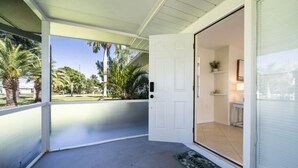 A covered porch with a white door leading to a room with a tiled floor and a small plant on a shelf. - Beautiful 2bd with River Views & Amazing Sunsets (Fort Myers)