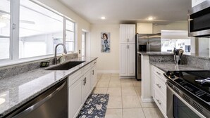 A modern kitchen with a granite countertop, stainless steel appliances, and a window providing natural light. - Beautiful 2bd with River Views & Amazing Sunsets (Fort Myers)