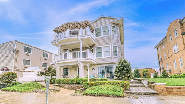 A multi-story residential building with a balcony, a covered porch, and a well-maintained garden. - Pineapple Pad:ACROSS from beach + boardwalk + parking w/ Full Linen Service! (Ocean City)