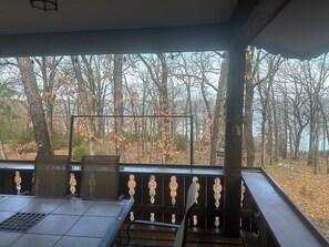 A covered outdoor seating area with a table and chairs, overlooking a forested area with autumn foliage.