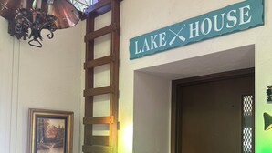 Una silla de madera, una escalera, una puerta con un letrero que dice "LAKE HOUSE" y un cuadro en la pared.