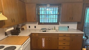 Una cocina con armarios de madera, una estufa blanca, un fregadero y una ventana con barrotes.