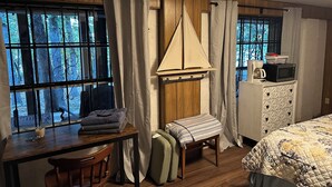 Una habitación acogedora con un escritorio de madera, una mesita, un banco, una cama y una ventana con cortinas.