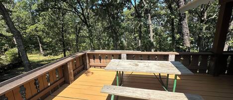 Una terraza de madera con una mesa de picnic y bancos, rodeada de árboles.