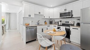 Una cocina moderna con armarios blancos, electrodomésticos de acero inoxidable y una zona de comedor con mesa y sillas.