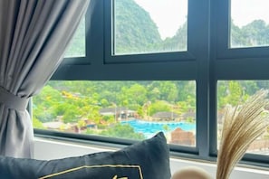 A window with a view of a pool and greenery, a black pillow with a gold outline, and a vase with dried plants. - Sunway Onsen Ipoh by EUcation Home (Ulu Kinta)